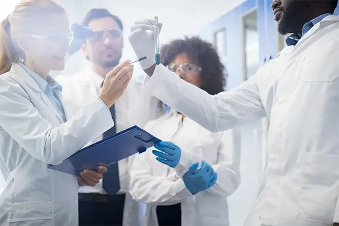 group-of-healthcare-professionals-in-labcoats-pointing-to-a-test-tube-662x442